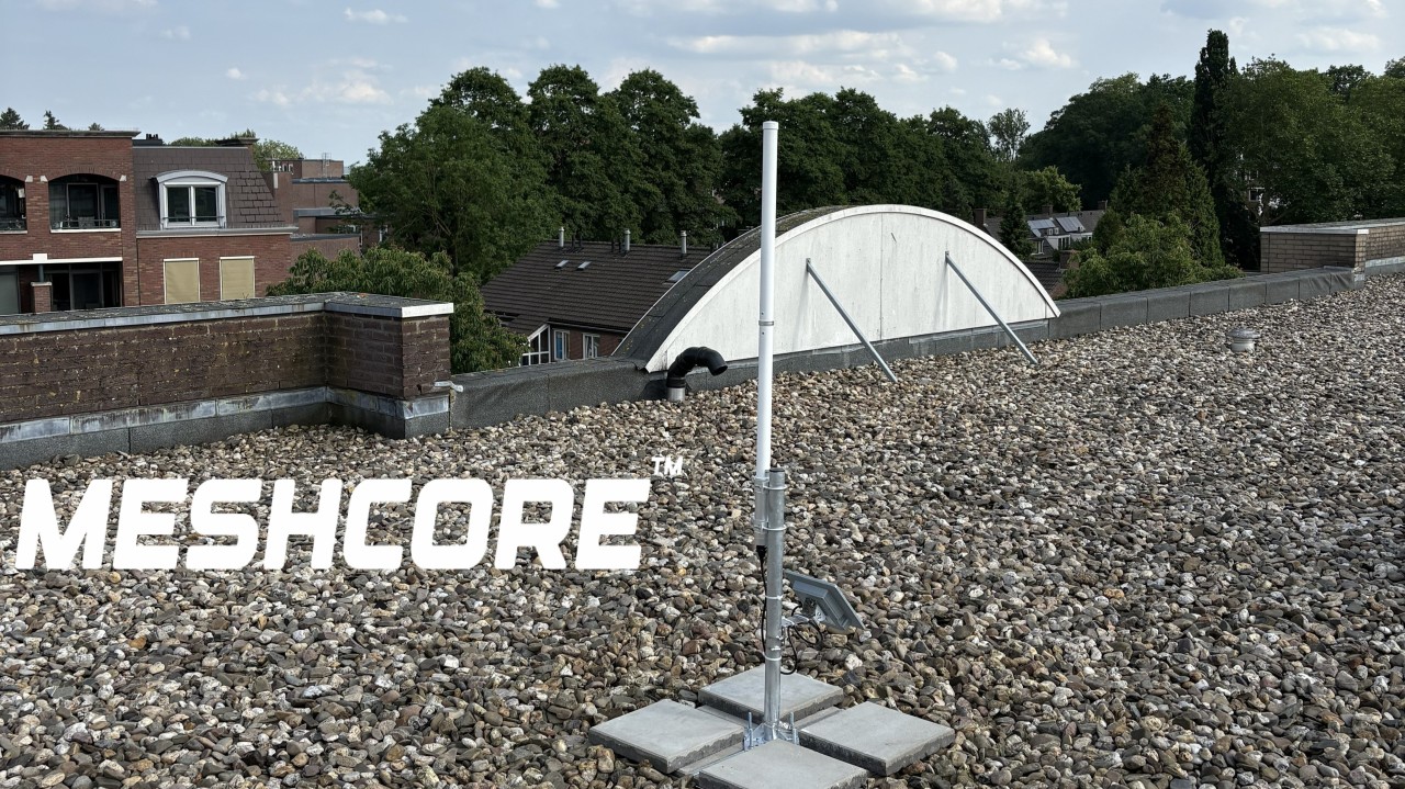 A MeshCore repeater and antenna on a ballasted rooftop mast in Zevenaar